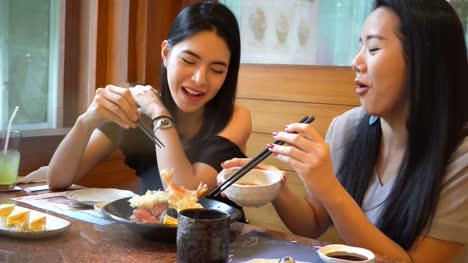 Two-Asian-female-friends-eating-and-having-a-meal-together.-Women-enjoying-good-time-at-Japanese-restaurant