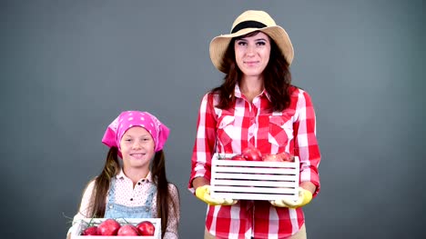 Retrato-de-familia-de-agricultores,-madre-e-hija-sosteniendo-en-sus-manos-las-cajas-de-madera-con-maduras-manzanas-orgánicas,-Sonriente,-sobre-un-fondo-gris-en-el-estudio
