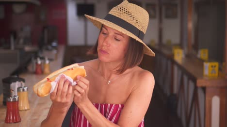Modern-woman-in-straw-hat-enjoying-tasty-hotdog