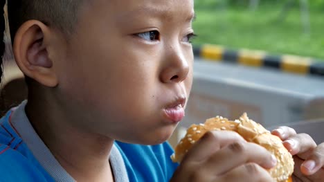 Close-up-little-asians-boy-enjoy-eating-burger,-Cute-happy-boy-holding-hamburger-at-restaurant.-video-Slow-motion