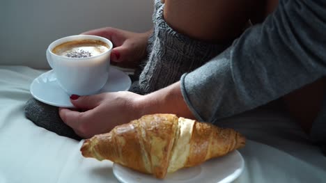 Woman-sitting-with-coffee-cup-and-croissant-on-couch-4K