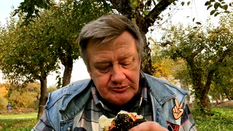 Hungry-adult-man,-in-casual-dress,-aged,-eats-hamburger-with-a-black-bun.
