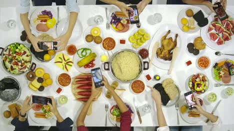 Group-of-friends-at-dinner-party-with-all-people-on-the-table-uses-their-smartphone-for-taking-photos-of-dinner-food.-Instagram,-Social-network-addiction-concept.