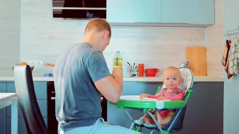 Hübscher-junger-Vater-Verfütterung-an-seine-Babynahrung-in-der-Küche