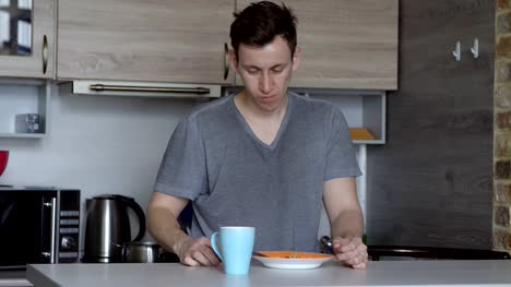 Young-man-eating-oatmeal-porridge-and-coffee-in-the-kitchen