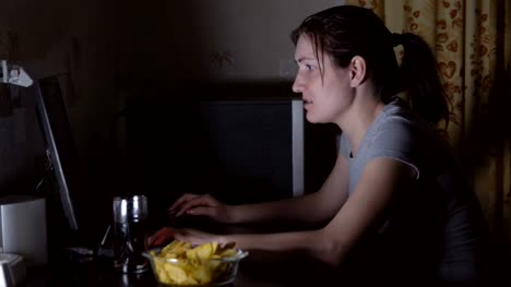 Young-woman-sitting-at-the-computer-and-eating-chips