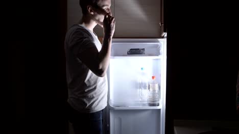 Young-man-eating-at-night-near-the-refrigerator