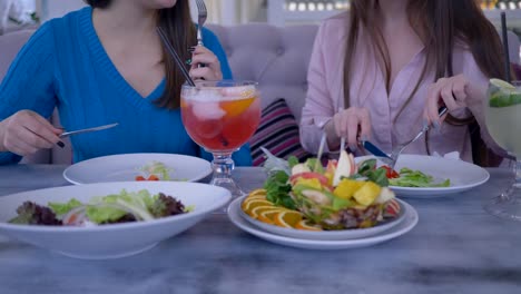 Diät-beginnen,-Mädchen-während-eines-Abendessens-mit-Gabel-und-ein-Messer-Essen-griechischen-Salat-im-Café-sitzen-am-Tisch-kommunizieren
