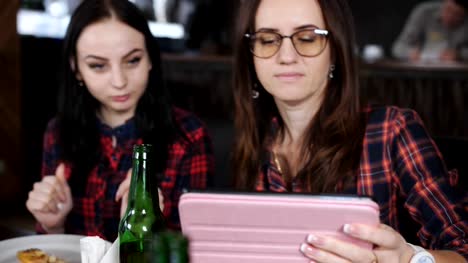 Cuatro-chicas-en-el-restaurante,-ver-las-fotos-en-el-tablet.-Pizza-y-cerveza-en-el-restaurante.