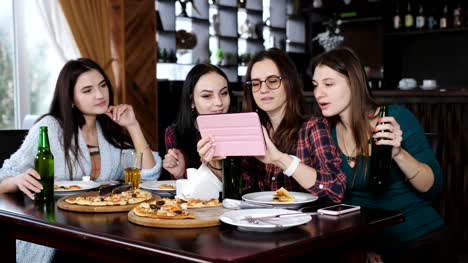 Spaß-Mädchen-sprechen-am-Tisch-im-Restaurant-und-Anzeigen-von-Fotos-auf-dem-Tablet.