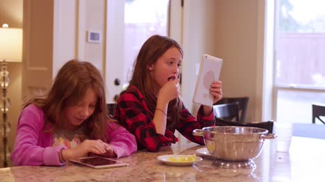Two-friends-sitting-at-a-kitchen-island-using-their-tablets-and-smiling-at-the-camera