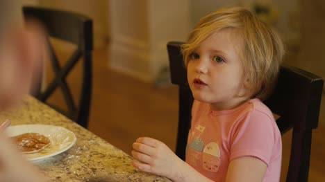A-little-girl-playing-with-her-pancakes-with-her-hands,-talking-and-smiling