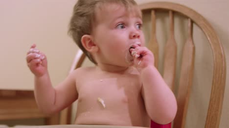 Ein-entzückender-kleiner-Junge-in-einem-Hochstuhl-Booster-Sitz-essen-chaotisches-Essen-mit-seinen-Händen