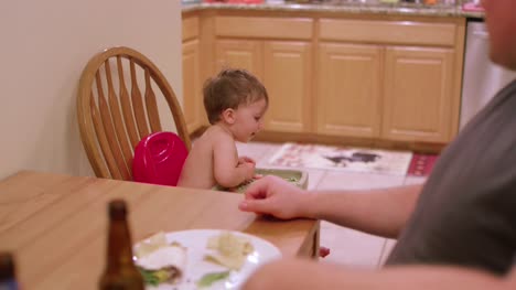An-adorable-little-boy-in-a-high-chair-booster-seat-eating-messy-food,-dinner-time-with-family