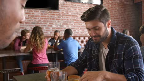 Two-Male-Friends-Eating-Out-In-Sports-Bar
