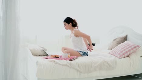 Young-brunette-woman-stretches-on-a-bed.-Beautiful-girl-using-laptop-during-breakfast.-Drinking-juice-and-dancing