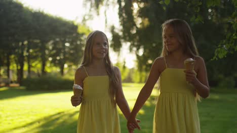 Two-Girls-are-Walking-at-Park-and-Holding-Ice-Cream-in-Hands