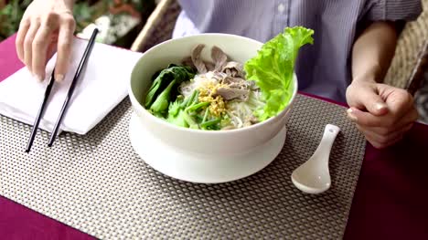 Woman-eat-traditional-Vietnam-Pho-Bo-(beef-noodle-soup)-with-chopsticks-in-restaurant.-Waiter-serve-soup-in-cafe.