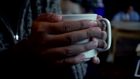 Frau-Hand-hält-eine-Tasse-Kaffee-im-Café-in-den-regnerischen-Tag