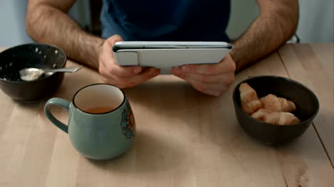 Hände-des-Mannes-hält-digital-Tablette-am-Frühstückstisch