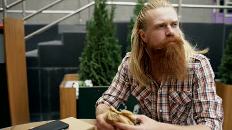 Bearded-student-man-eating-burger-in-street-cafe-outdoors