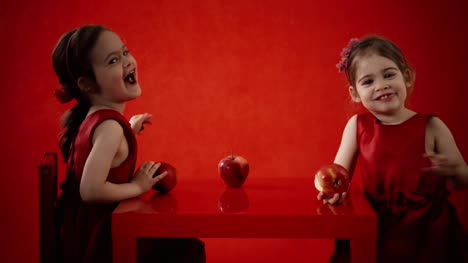 Zwei-kleine-Mädchen-essen-Äpfel-auf-einem-roten-Tisch