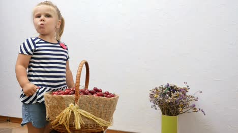 Little-girl-tries-a-cherry-from-basket,-shows-a-thumb-up-and-winks