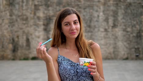 Cute-Young-Woman-Eating-With-A-Spoon-From-A-Cup-Ice-Cream-On-The-Street