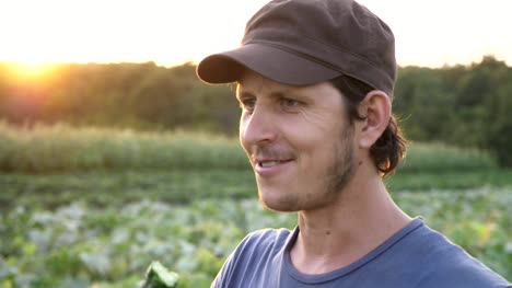 Farmer-standing-at-field-of-organic-farm,-eating-fresh-ripe-cucumber-and-smiling