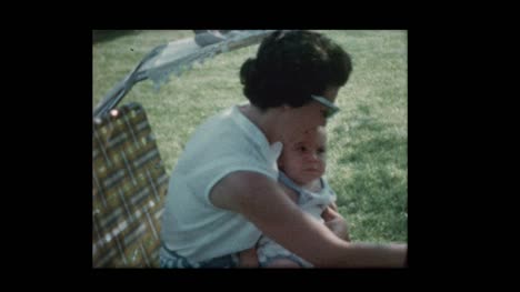 Mom-feeds-baby-sitting-outside-on-lawn-chair-1960