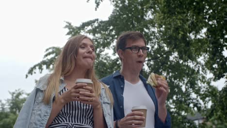 Young-Couple-Eating-Burger-and-Drinking-Coffee-during-Walk
