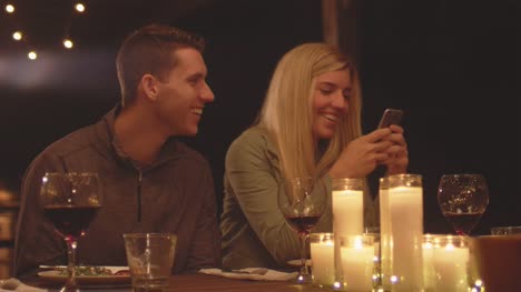 Joven-pareja-amoroso-mirando-su-teléfono-celular-mientras-que-en-una-mesa