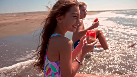 Jungen-und-Mädchen-essen-Wassermelone-am-Strand