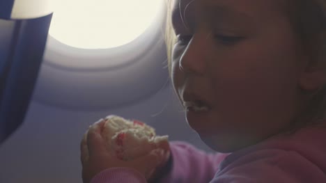 Close-up-child-girl-eat-burger-with-appetite-over-porthole-in-airplane