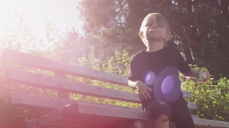 Little-kid-eating-bread-on-a-bench-at-the-park.-Lense-flare
