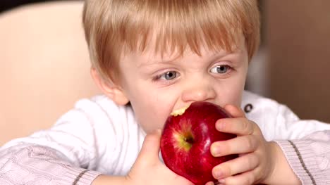 Kleines-Kind-beißt-roten-Apfel-am-Tisch-sitzen.
