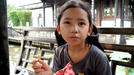 Linda-niña-asiática-comer-snack-con-felicidad