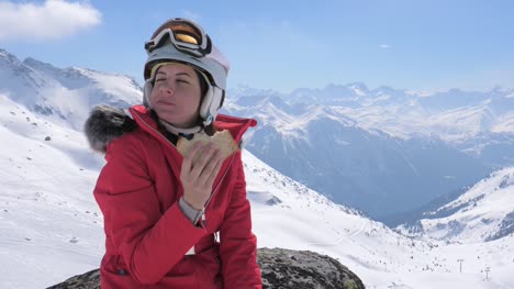 Esquiador-de-la-mujer-se-sienta-en-una-piedra-en-el-centro-de-esquí-de-las-montañas-y-come-un-sándwich