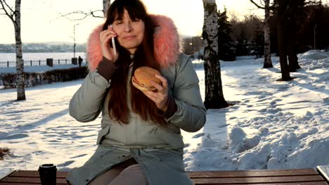 Junge-Frau-isst-einen-Burger-auf-Winter-Straße