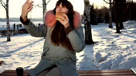 Young-woman-eats-a-burger-on-winter-street
