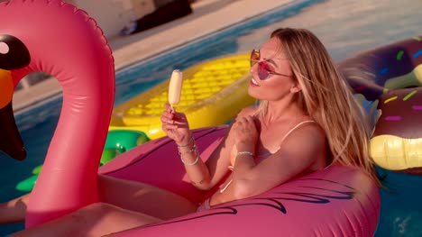 Woman-in-pool-eating-ice-cream-and-floating-on-inflatable-flamingo