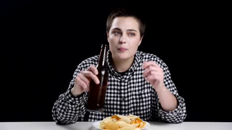 Mannish-Mädchen-trinkt-Bier,-Thhinking,-Kartoffelchips-auf-Teller,-Diät-Konzeption,-schwarzen-Hintergrund-50fps