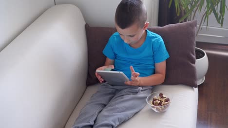 Handsome-boy-sitting-on-couch-and-using-tablet-at-home