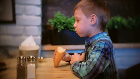 Junge-isst-eine-Baguette-und-schaut-TV-im-Café.-Seitenansicht.
