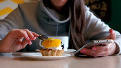 Unrecognizable-woman-eats-a-cake-with-a-spoon-and-looks-at-the-phone-screen.-Close-up.