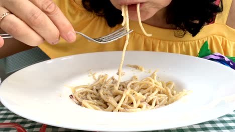 Frau-in-einem-gelben-Kleid-ist-eine-Pasta-mit-weißer-Soße-Essen.