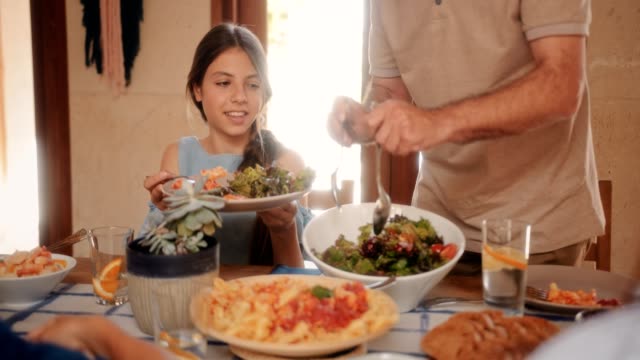 Abuelo-que-sirve-a-nieta-mediterránea-ensalada-en-el-almuerzo-familiar