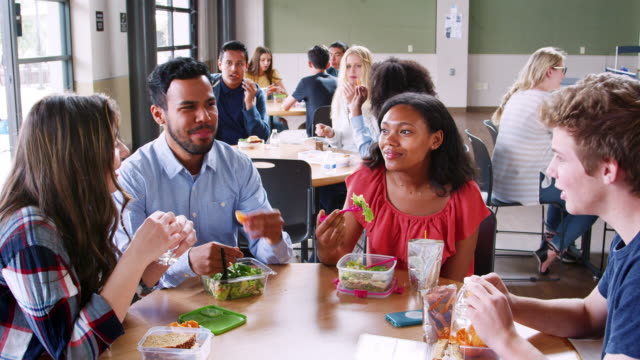 Teacher-And-Students-Eating-Lunch-In-High-School-Cafeteria-During-Recess