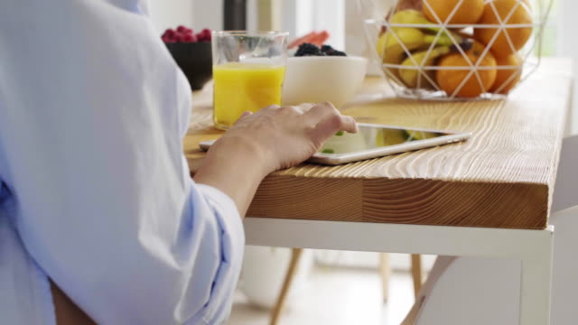 Frau-mit-einem-Tablet-und-trinken-Orangensaft-in-Küche