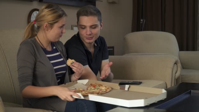 Hermosa-pareja-jóvenes-sentados-en-el-sofá-y-comer-pizza